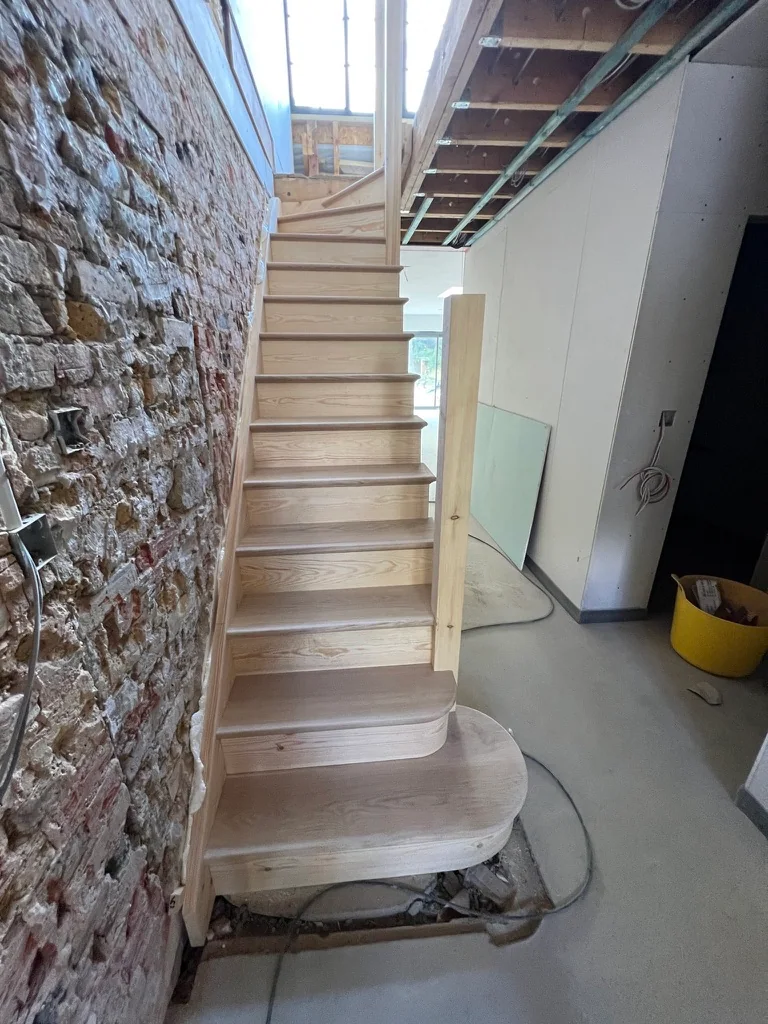 Unfinished timber staircase fitted beside an exposed brick wall