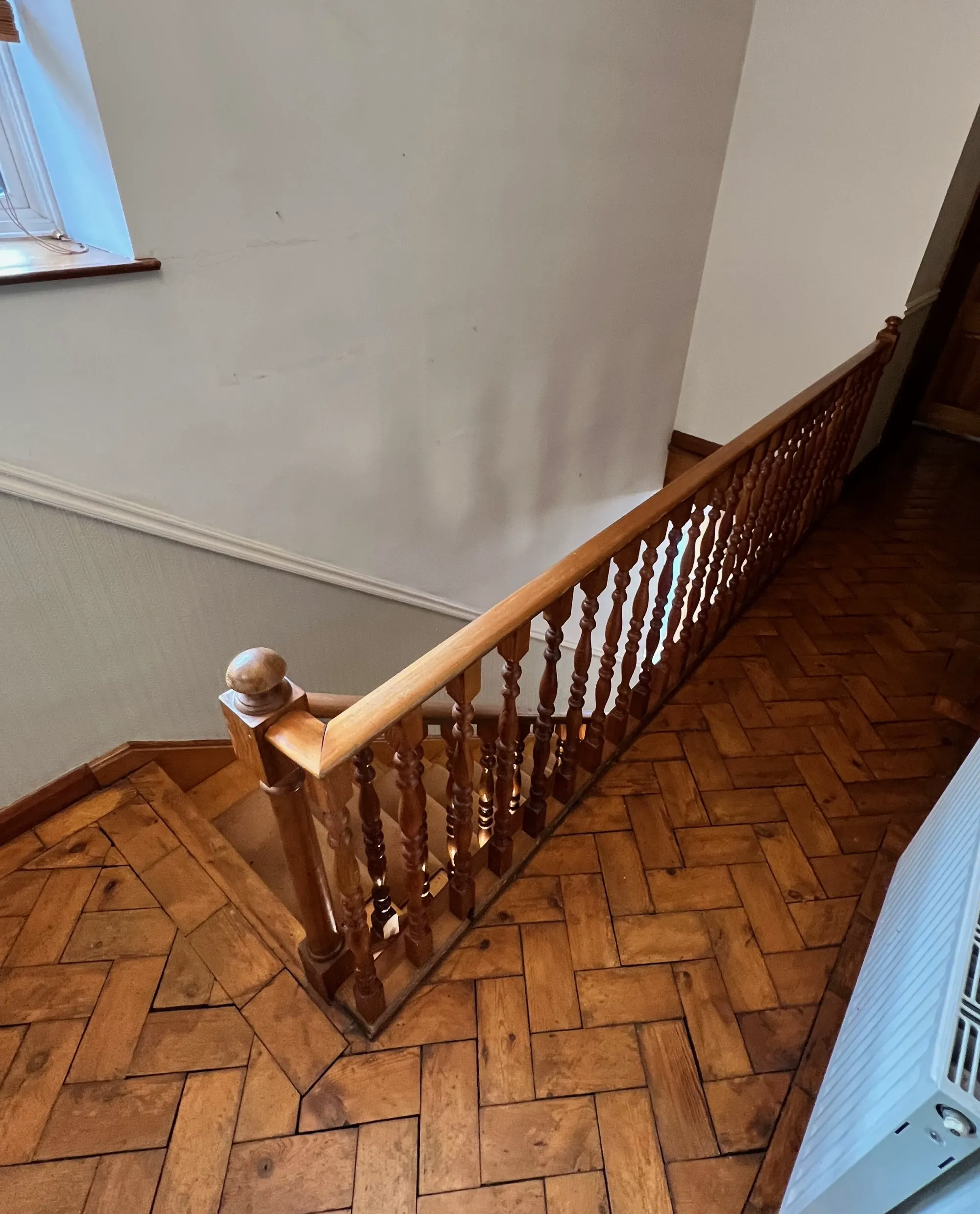 A landing staircase with traditional turned spindles and a wooden handrail before a modern safety upgrade.