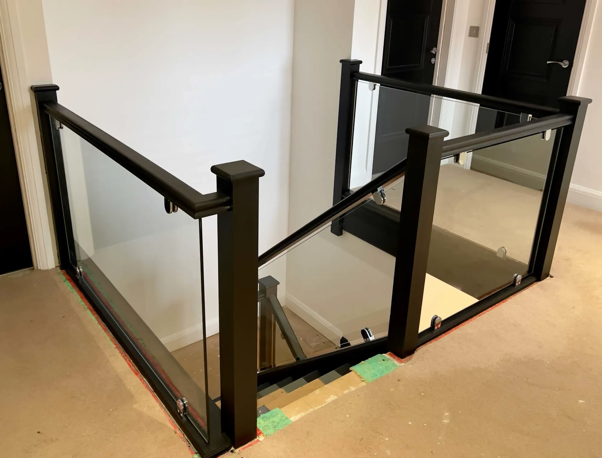 Contemporary black staircase balustrade with glass panels and chrome brackets, showcasing elegant modern craftsmanship.