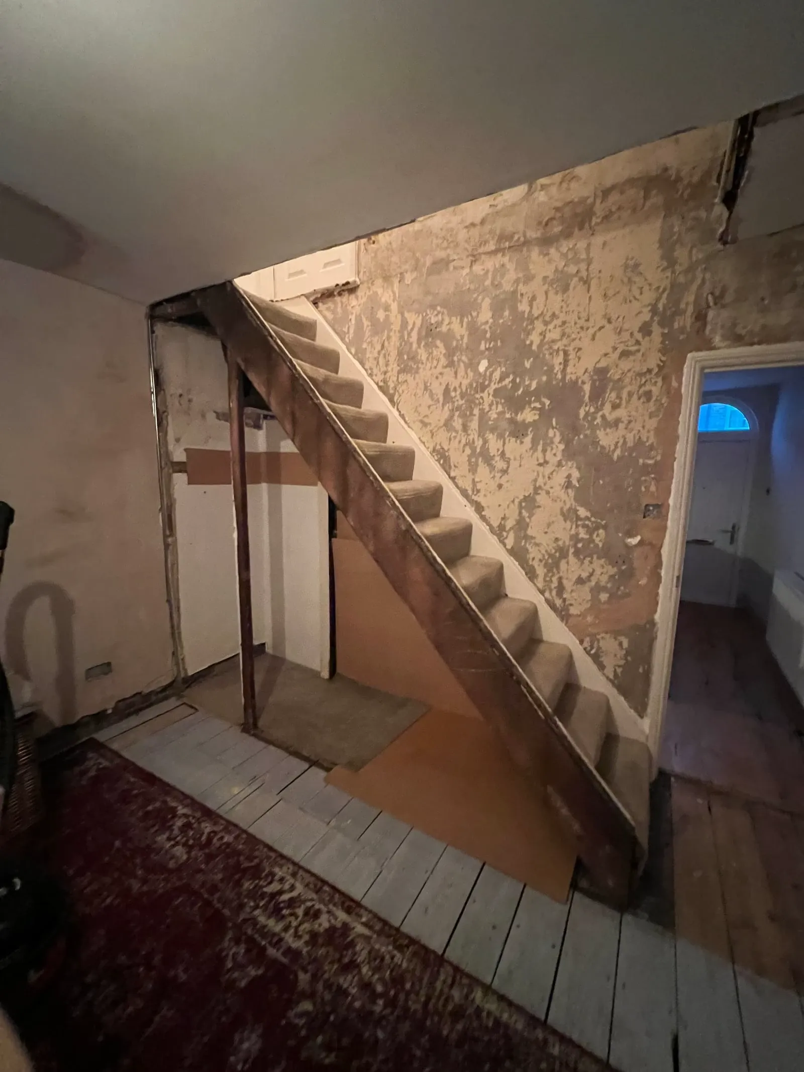 A worn, carpeted staircase in a partially stripped-down room, showing the space before renovation.