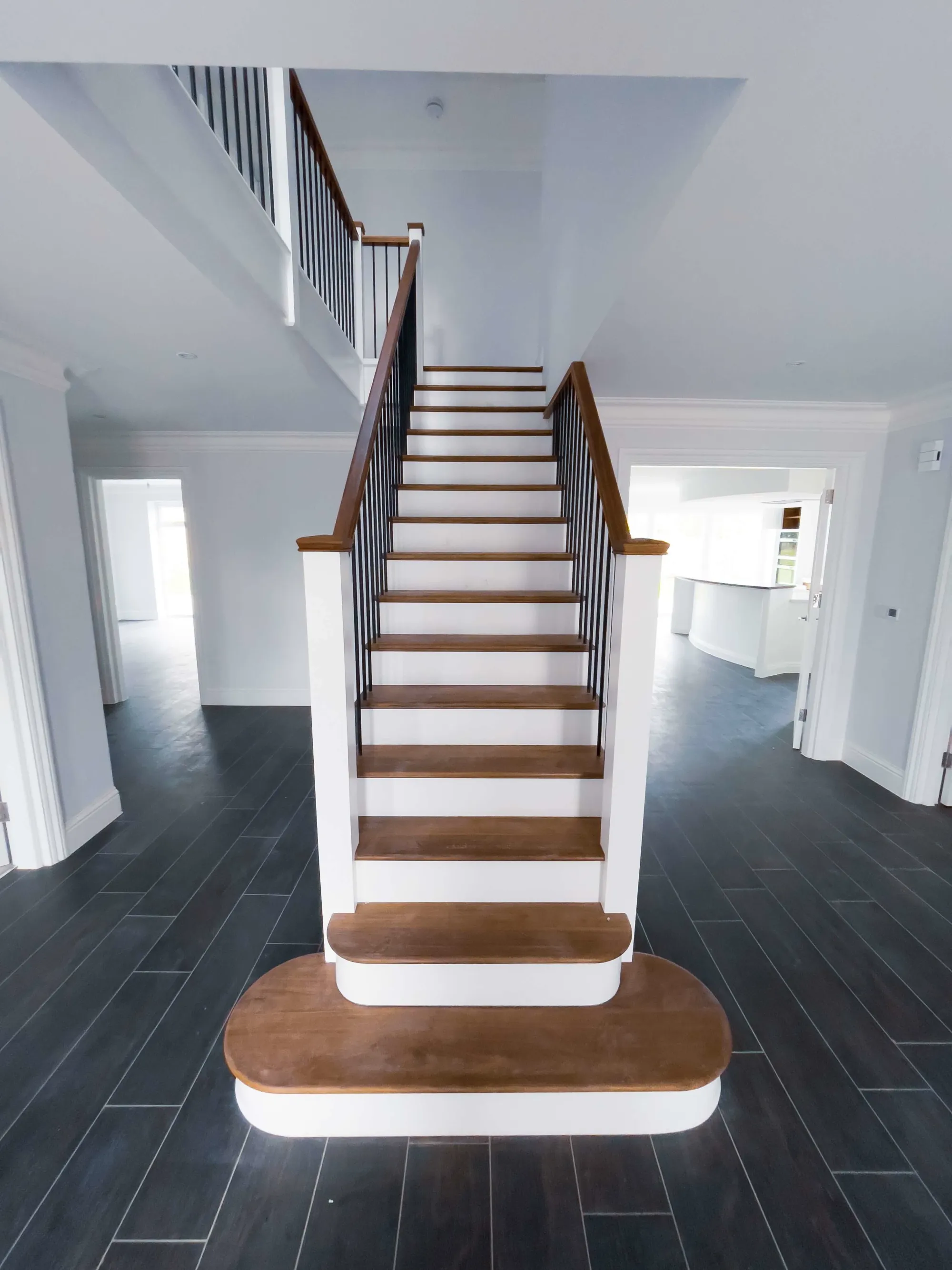 Straight-on view of a bespoke staircase with American Black Walnut treads, minimalist handrails, and round black spindles in a Bromley new build.