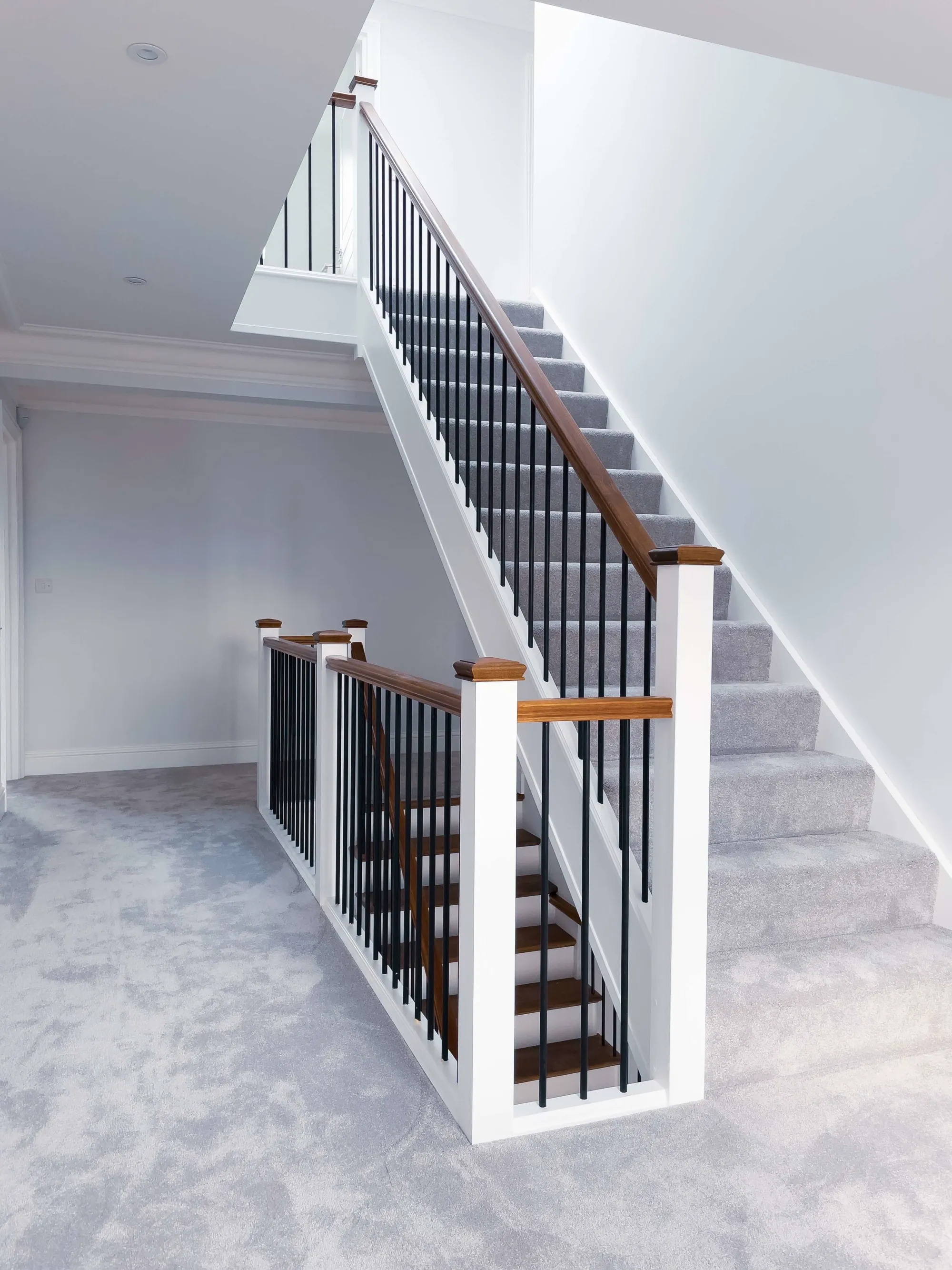 Straight-on view of a bespoke staircase with American Black Walnut treads, minimalist handrails, and round black spindles in a Bromley new build.