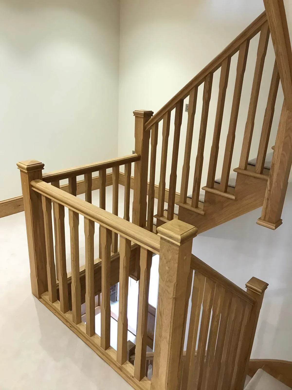 A wooden staircase with beige carpeted steps, wooden balustrades. Cream-painted walls surround it.