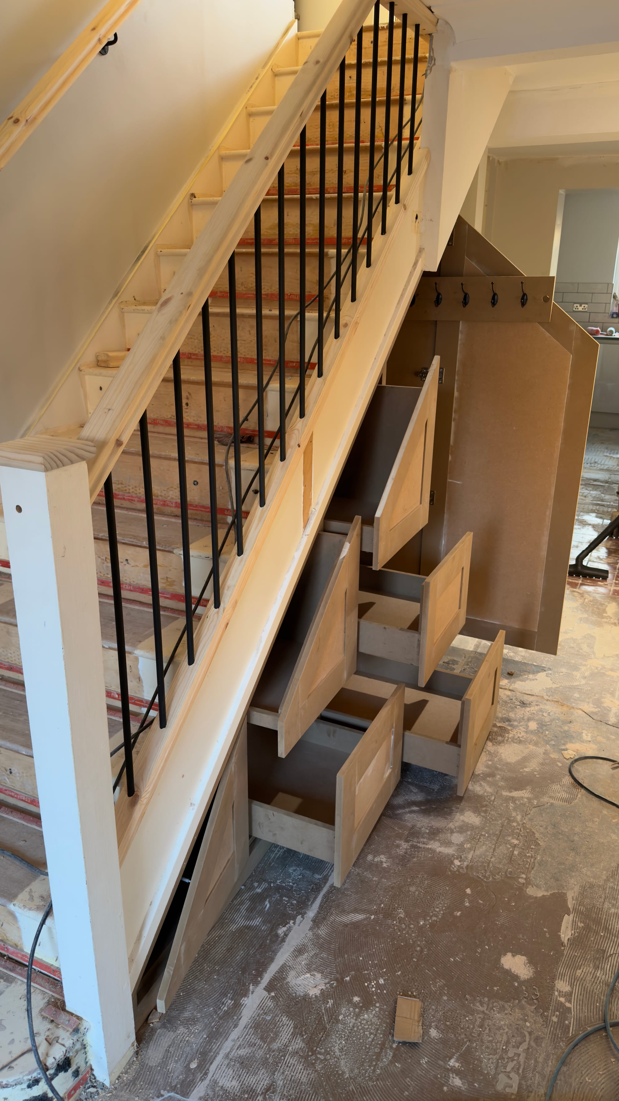 Custom under-stairs storage in Kent with shaker drawers, coat hooks and tall cupboard built into a staircase renovation.