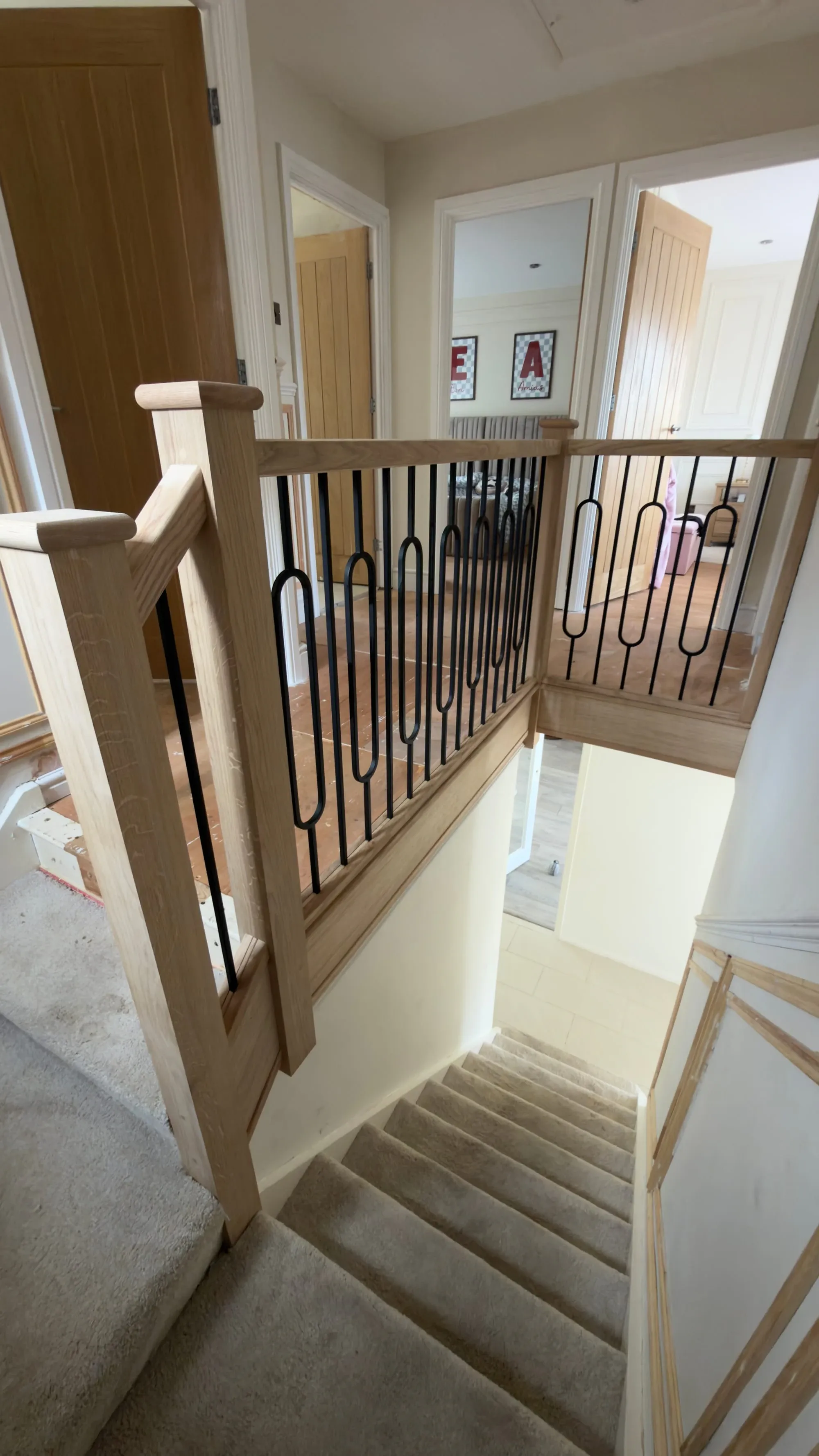 Renovated landing with clear-varnished timber posts, rounded newel caps, black metal spindles and matching timber apron cladding.