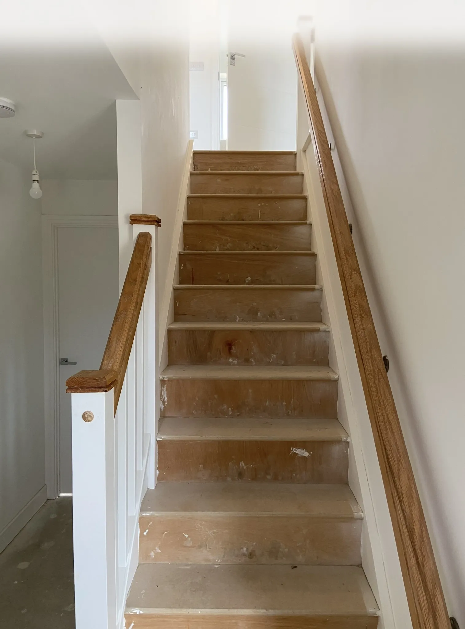 Staircase before cladding, with bare steps and a pine plug visible in the bottom newel post.