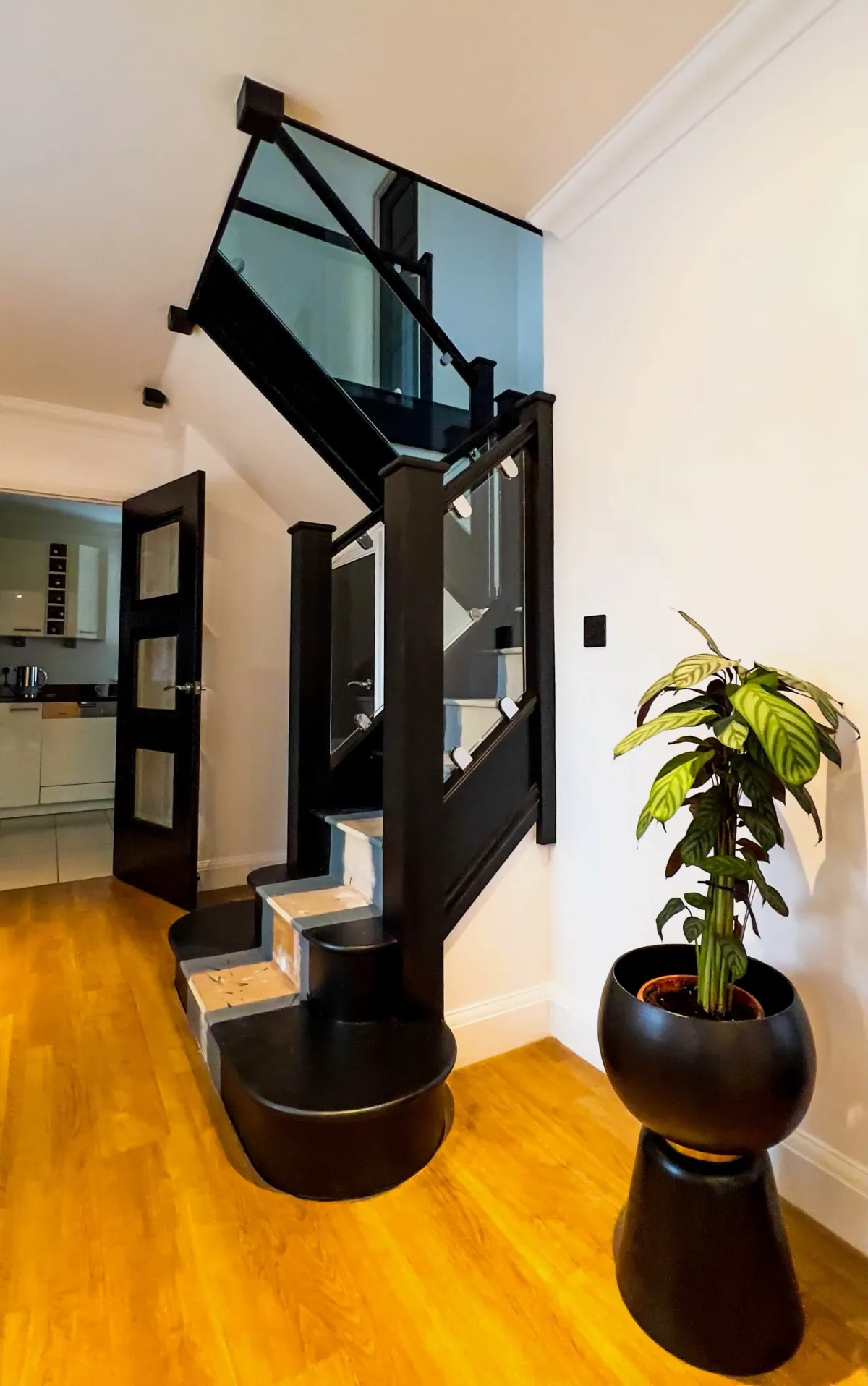 Modern black staircase with toughened glass panels, chrome brackets, and wooden flooring, designed for a sleek upgrade.