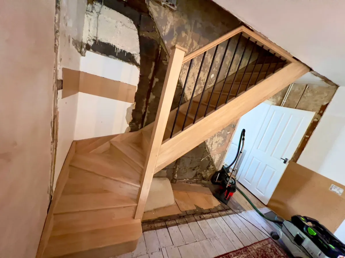 A modern oak staircase with black metal spindles, partially installed in a room mid-renovation.