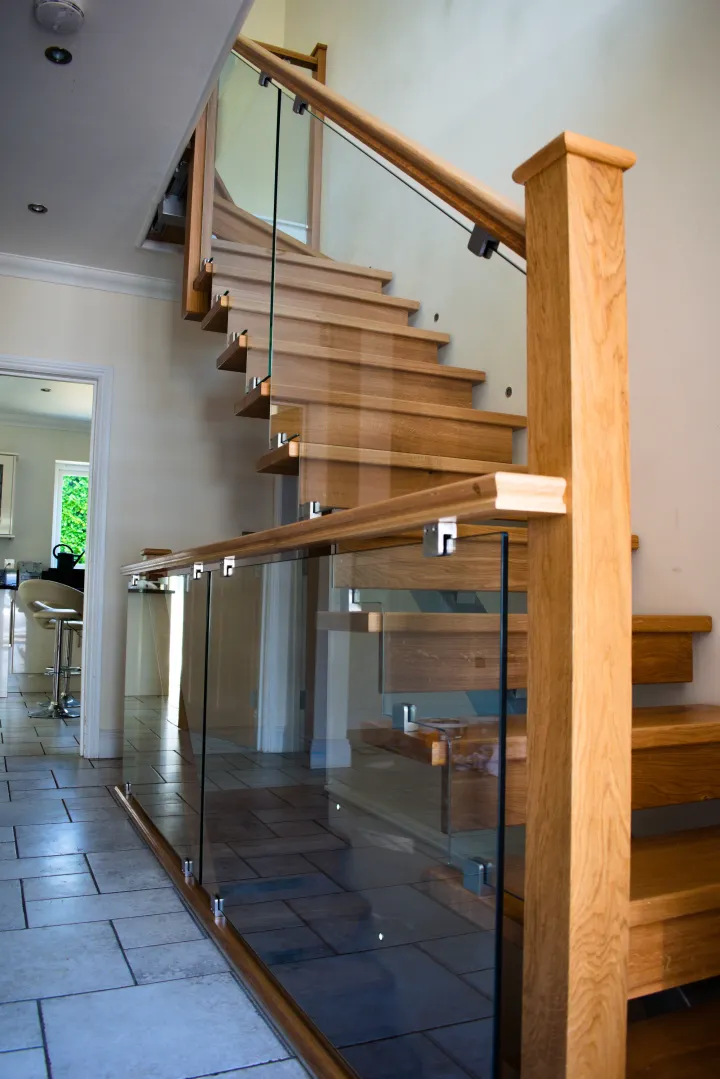 A wooden staircase with glass balustrade next to a tiles floor.