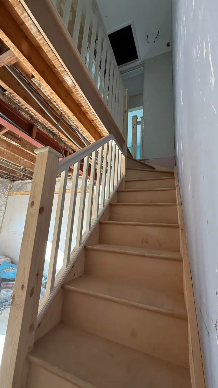 Upward view of a wooden staircase with a white balustrade leading to a landing. Bespoke stair design and installation in Kent