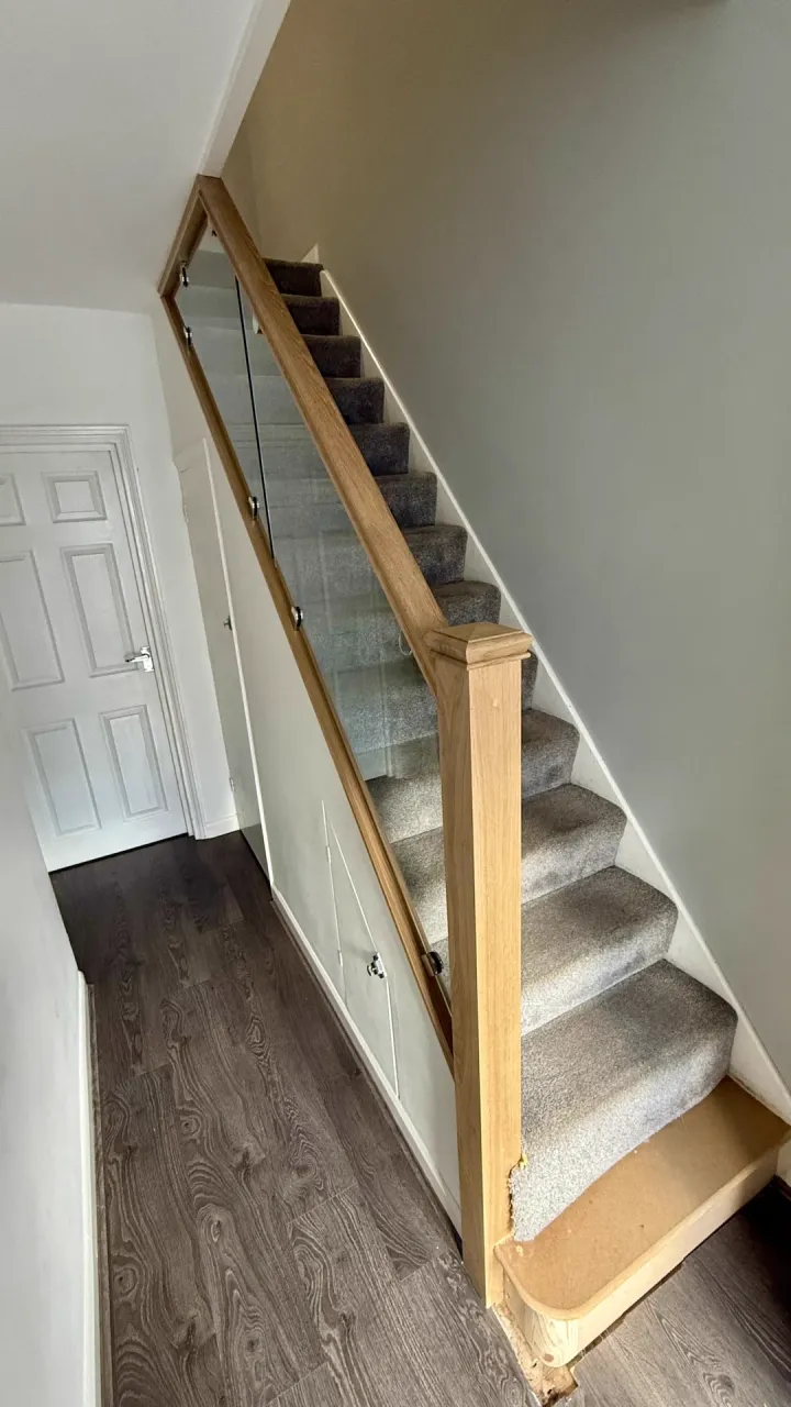 Glass staircase refurbishment in Kent featuring oak handrail, modern balustrades and precise staircase renovation detailing.